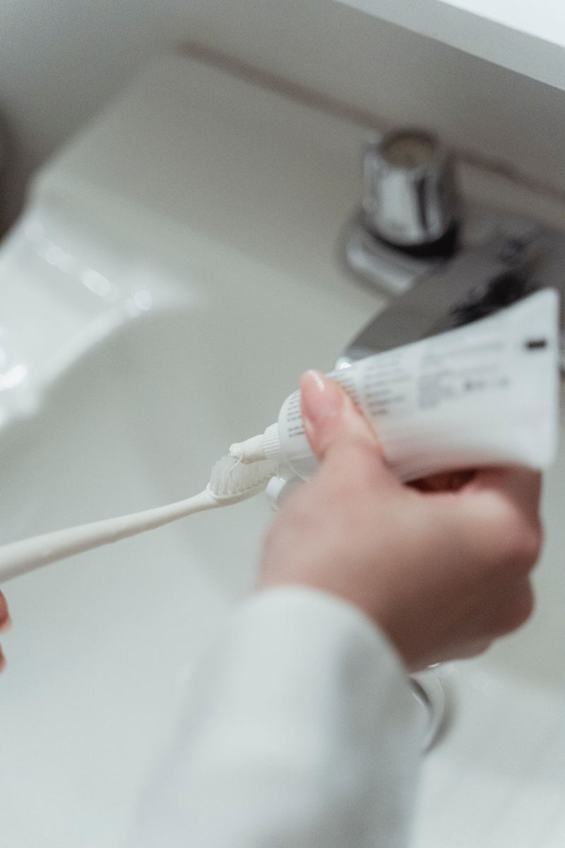 Main déposant du dentifrice sur une brosse à dents, symbole de la routine dentaire de la rentrée