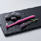 End-tuft toothbrush — on a wet black slate with pebbles and lavender