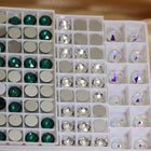 Cristaux taillés à dos plat rangés par teinte dans des plateaux à compartiments : émeraude, cristal et cristal irisé