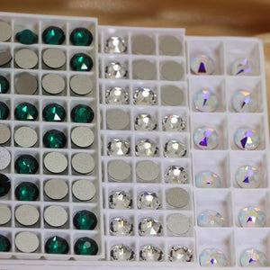 Cristaux taillés à dos plat rangés par teinte dans des plateaux à compartiments : émeraude, cristal et cristal irisé