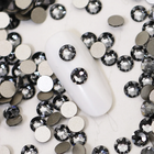 Cristaux à dos plat gris fumé, face taillée et dos argenté visibles, autour d’une capsule d’ongle de démonstration
