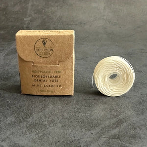 Boîte en carton kraft de fil dentaire 50 m parfum menthe, à côté d’une bobine de fil blanc