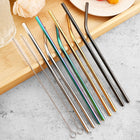 Straws in mixed finishes with their cleaning brushes, on a wooden tray