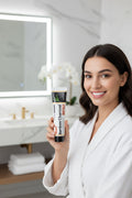 Femme en peignoir présentant le dentifrice Charbon Actif Blancheur ÉclatDent dans une salle de bain