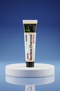 Dentifrice Charbon Actif Blancheur ÉclatDent sur un socle rond, fond studio bleu dégradé