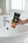 Main tenant le dentifrice Blancheur Douceur Coco ÉclatDent au-dessus d'un lavabo de salle de bain