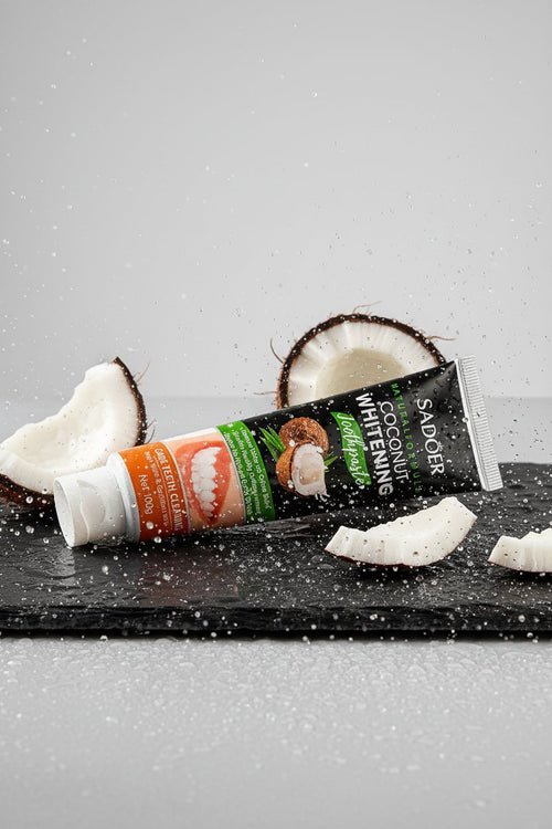 Dentifrice Blancheur Douceur Coco ÉclatDent sur une ardoise humide avec des morceaux de noix de coco