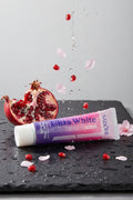 Dentifrice Grenade & Sakura ÉclatDent sur une ardoise humide avec grenade ouverte et pétales de cerisier
