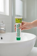 Main tenant le dentifrice Classique Menthe ÉclatDent au-dessus d'un lavabo de salle de bain