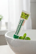 Dentifrice Classique Menthe ÉclatDent posé sur un lavabo blanc avec des feuilles de menthe