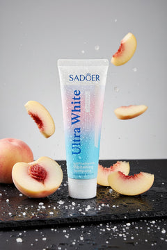 Peach & Sea Salt Multi-Action ÉclatDent toothpaste on a wet slate with fresh peach slices