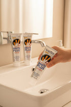Pack Anti-Taches Tabac ÉclatDent : un tube tenu au-dessus d'un lavabo blanc, salle de bain lumineuse et robinet chrome