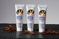 Pack Antimacchie Tabacco — 3 dentifrici ÉclatDent: i tre dentifrici SADOER distesi su ardesia nera bagnata di gocce d'acqua, con foglie di tabacco essiccate