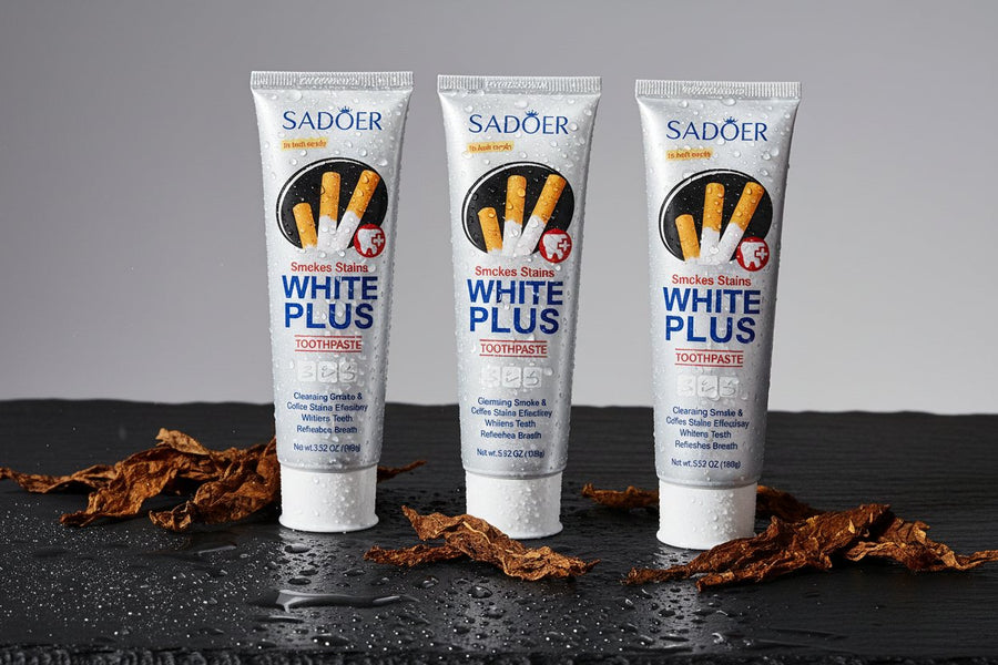 Pack Anti-Taches Tabac ÉclatDent : les trois dentifrices SADOER couchés sur une ardoise noire humide couverte de gouttes d'eau, avec feuilles de tabac séchées