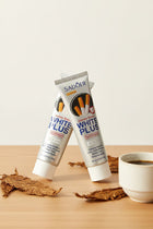 Pack Anti-Taches Tabac ÉclatDent : les trois tubes posés sur une table en bois clair avec des feuilles de tabac séchées et une tasse de café