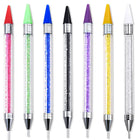 Sept stylos à cire alignés : manches transparents garnis de strass colorés, embouts cire de couleur et pointes métalliques
