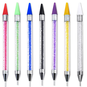Sept stylos à cire alignés : manches transparents garnis de strass colorés, embouts cire de couleur et pointes métalliques