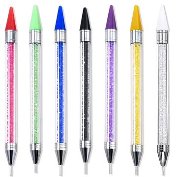 Sept stylos à cire alignés : manches transparents garnis de strass colorés, embouts cire de couleur et pointes métalliques