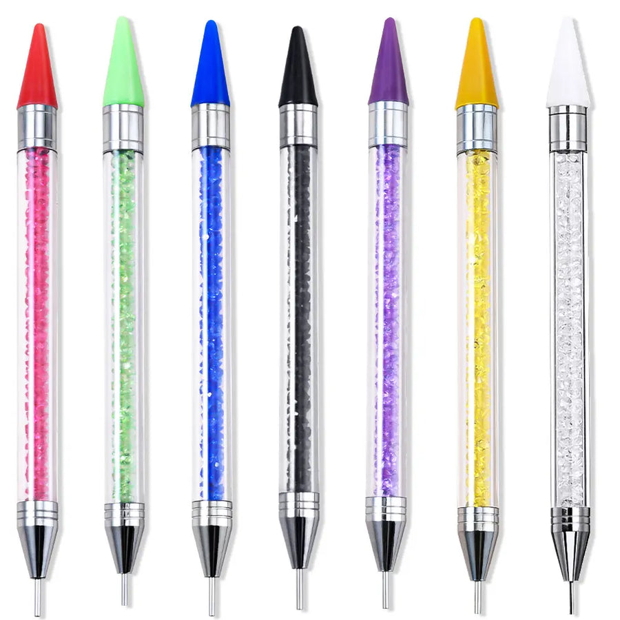 Sept stylos à cire alignés : manches transparents garnis de strass colorés, embouts cire de couleur et pointes métalliques