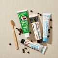 Pack Caffè-Dipendente — 4 dentifrici ÉclatDent visto dall'alto su sfondo beige: i quattro tubetti circondati da chicchi di caffè tostato