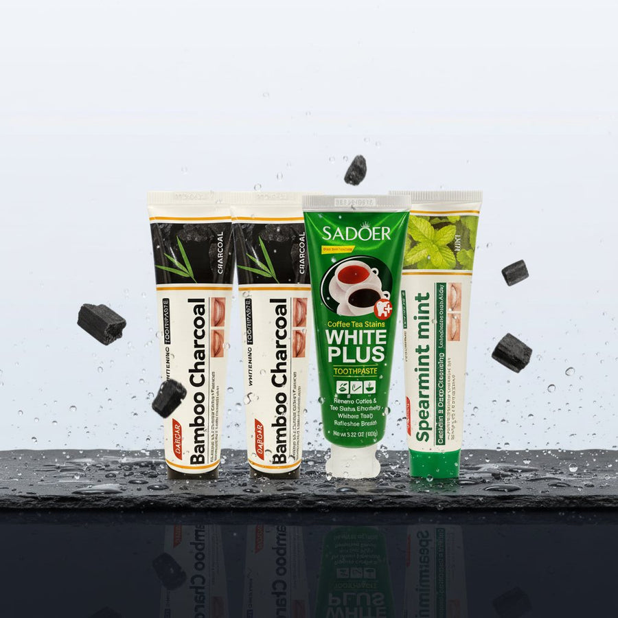 Pack Splendore Carbone — 4 dentifrici ÉclatDent: i quattro dentifrici SADOER distesi su ardesia nera bagnata di gocce d'acqua, con frammenti di carbone attivo