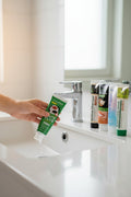 Complete Collection Pack — 8 toothpastes ÉclatDent: one tube held above a white washbasin, bright bathroom and chrome tap