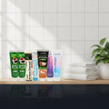 Complete Collection Pack — 8 toothpastes ÉclatDent: the eight tubes standing in a row on a light wooden bathroom shelf with folded white towels and a green plant