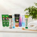 Complete Collection Pack — 8 toothpastes ÉclatDent: the eight tubes on a white marble tray with a wooden toothbrush and a soft towel