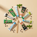 Complete Collection Pack — 8 toothpastes ÉclatDent seen from above on a beige background: the eight tubes surrounded by mint leaves and coffee beans, arranged in a fan