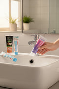 Pack Gengive & Dolcezza — 3 dentifrici ÉclatDent: un tubetto tenuto sopra un lavabo bianco, bagno luminoso e rubinetto cromato