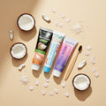 Pack Gengive & Dolcezza — 3 dentifrici ÉclatDent visto dall'alto su sfondo beige: i tre tubetti circondati da cocco, cristalli di sale e petali di ciliegio
